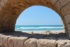 View through stone archway onto blue beach